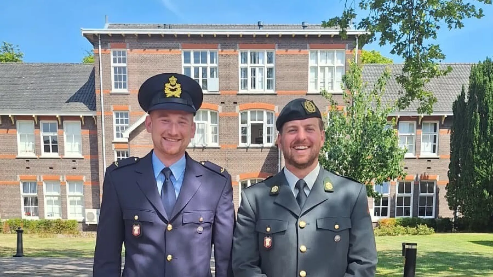 Twee mannen in militaire uniformen poseren buiten voor een gebouw.