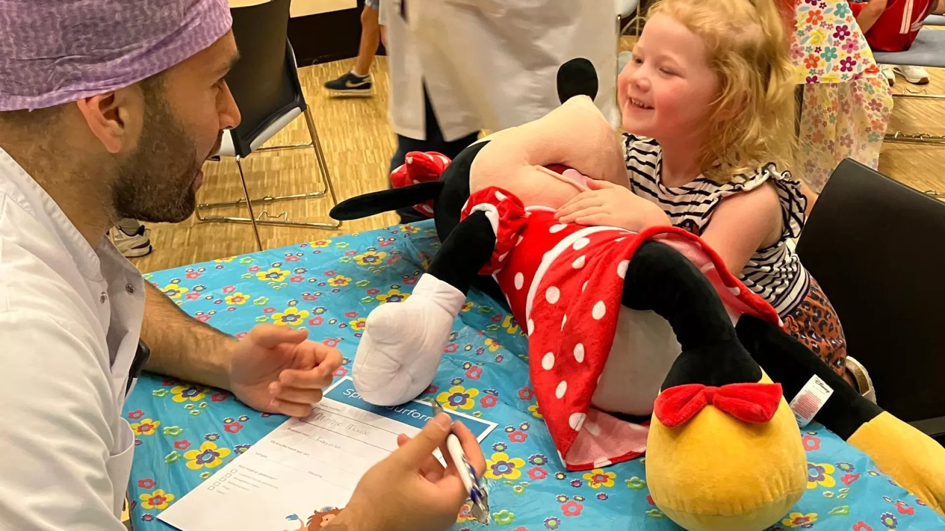 Een co-assistent in gesprek met een lachend meisje en een grote Minnie Mouse-knuffel.