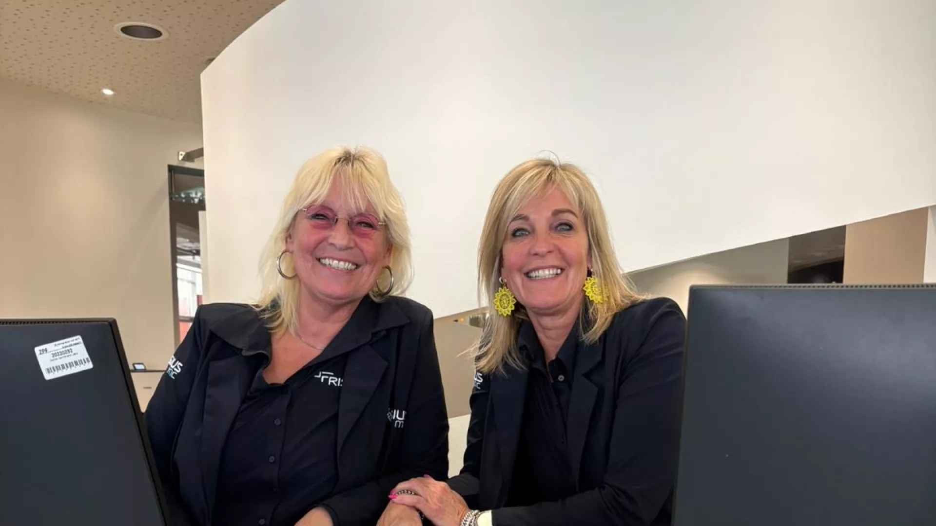 Twee medewerkers glimlachend achter de ontvangstbalie.