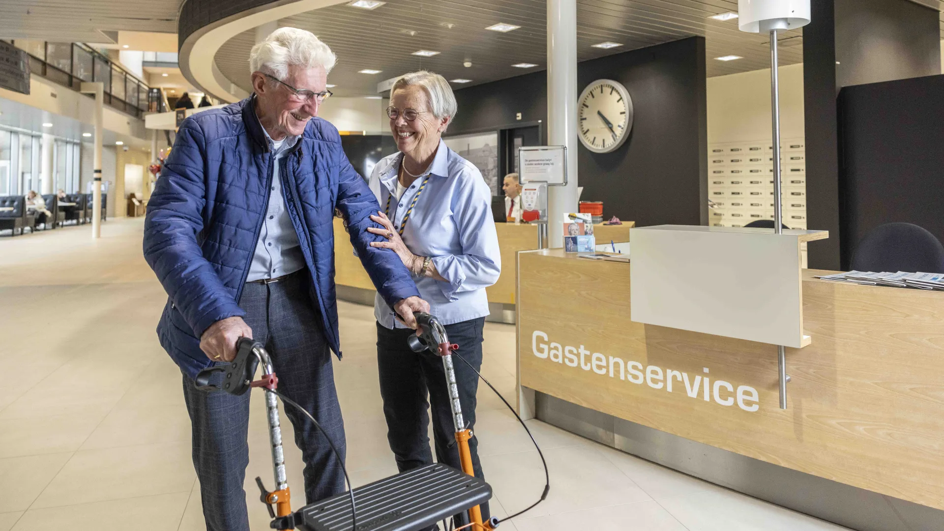 Oudere man met rollator krijgt hulp bij gastenservice.