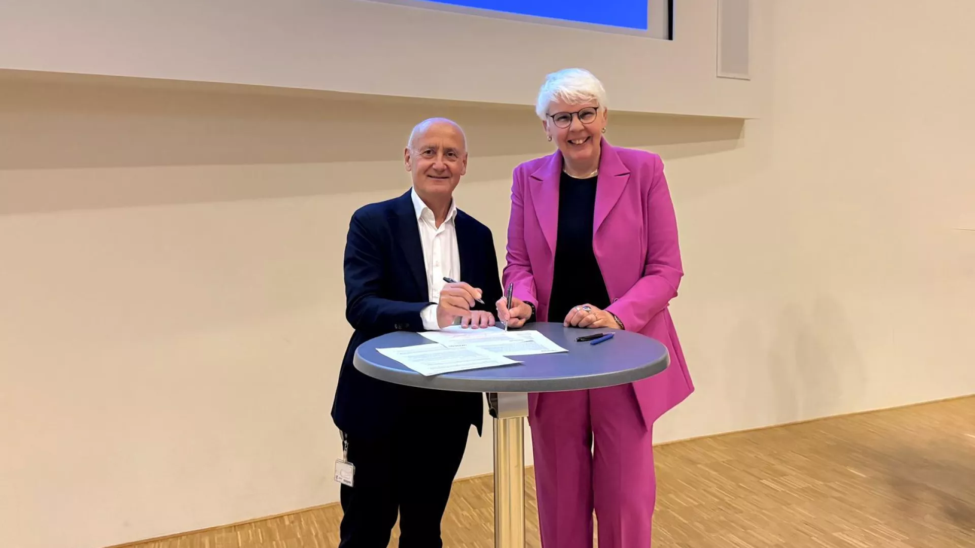 Twee bestuurders poseren samen bij een hoge tafel bij een ondertekenmoment.
