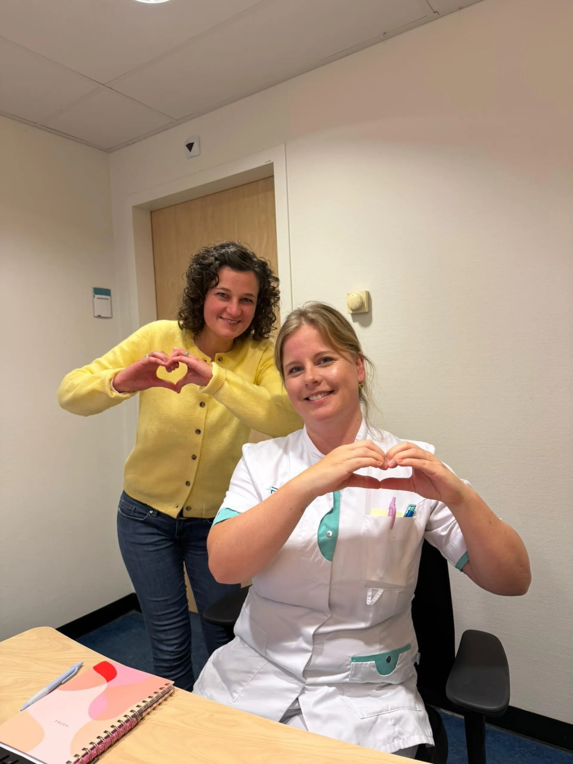 Twee vrouwen vormen hartvormige handgebaren in een kamer.