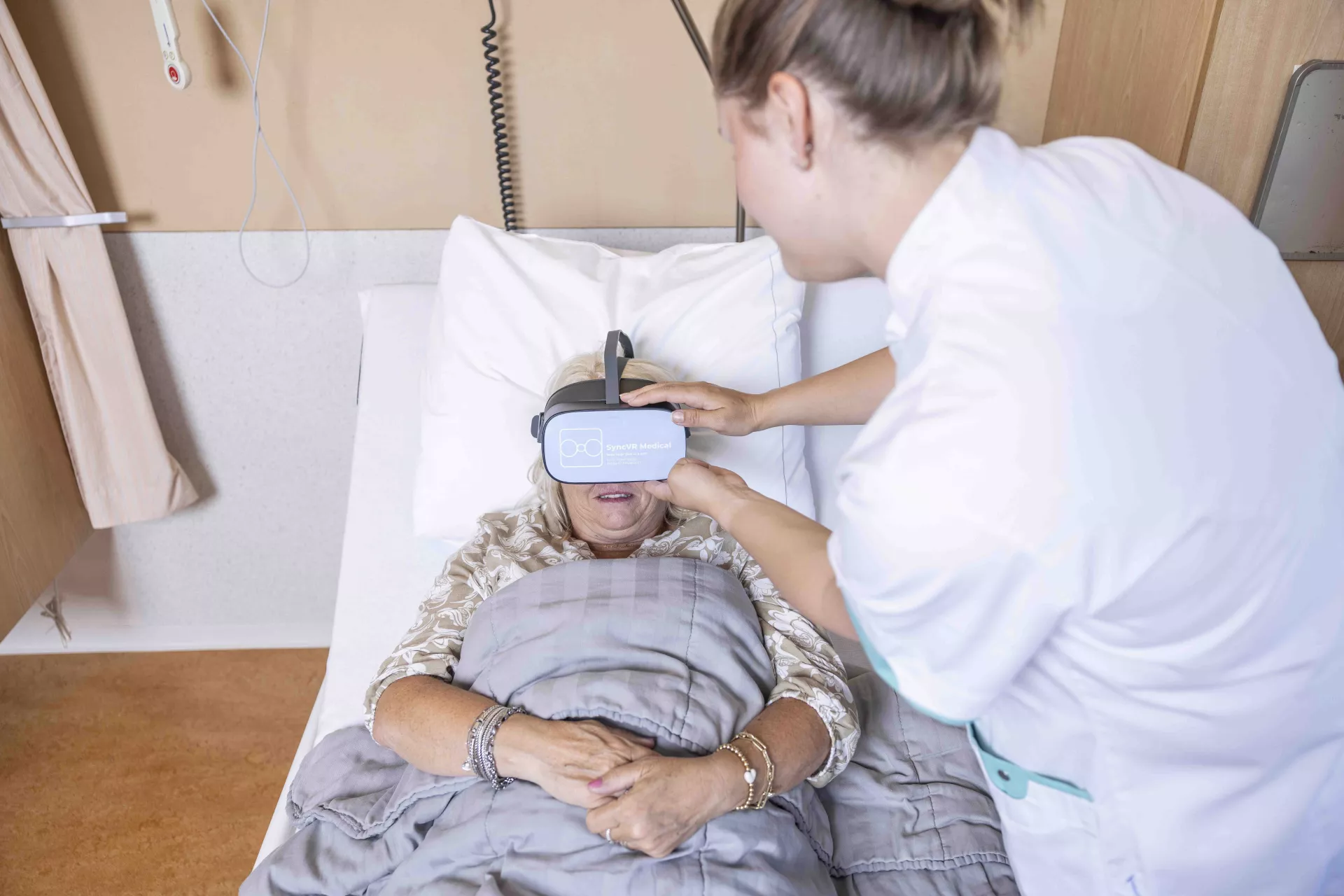 Verpleegkundige helpt patiënt bij het gebruik van een VR-headset in bed.