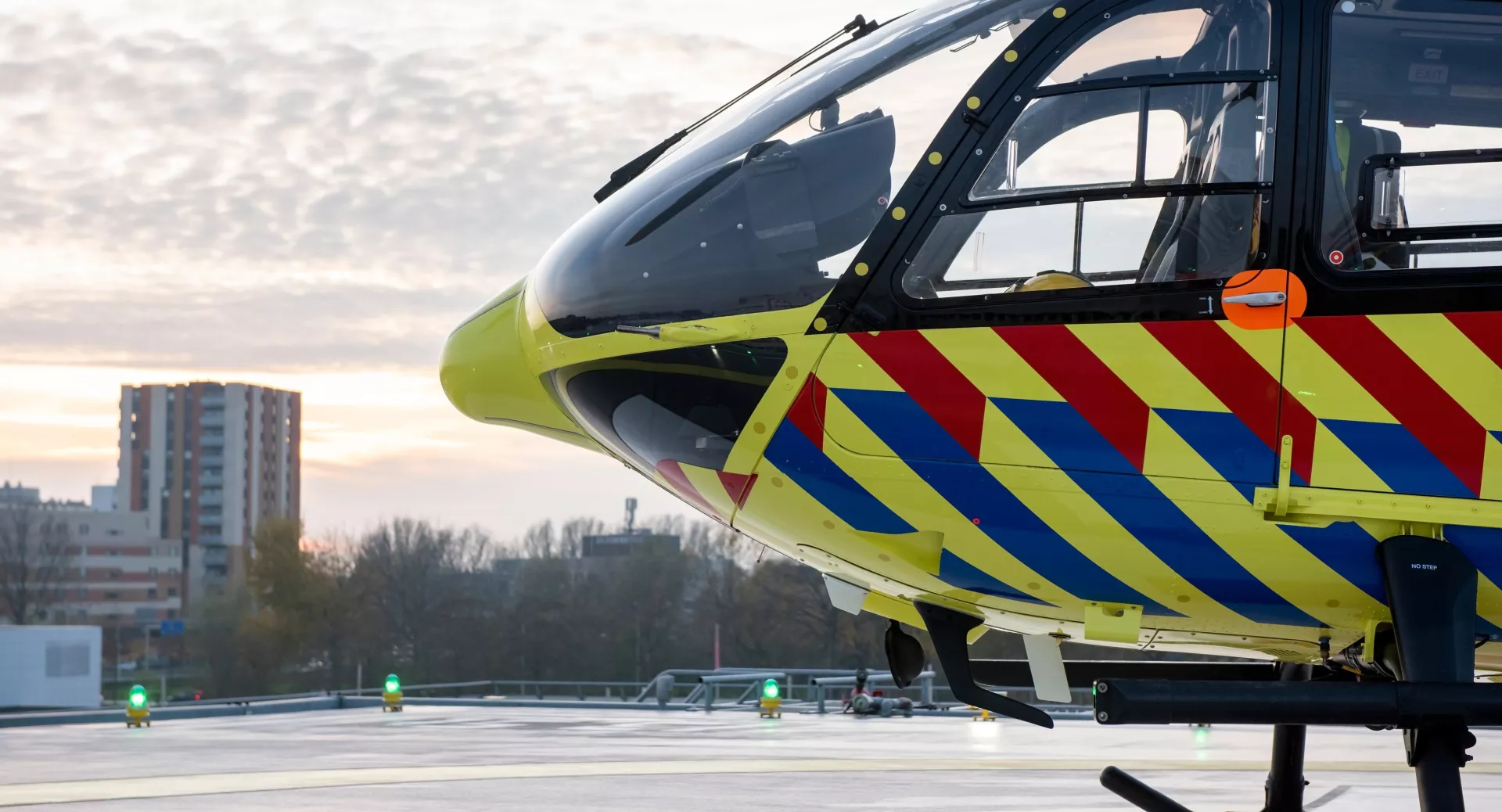 Helikopter met gekleurde strepen op een helikopterplatform bij zonsopgang.