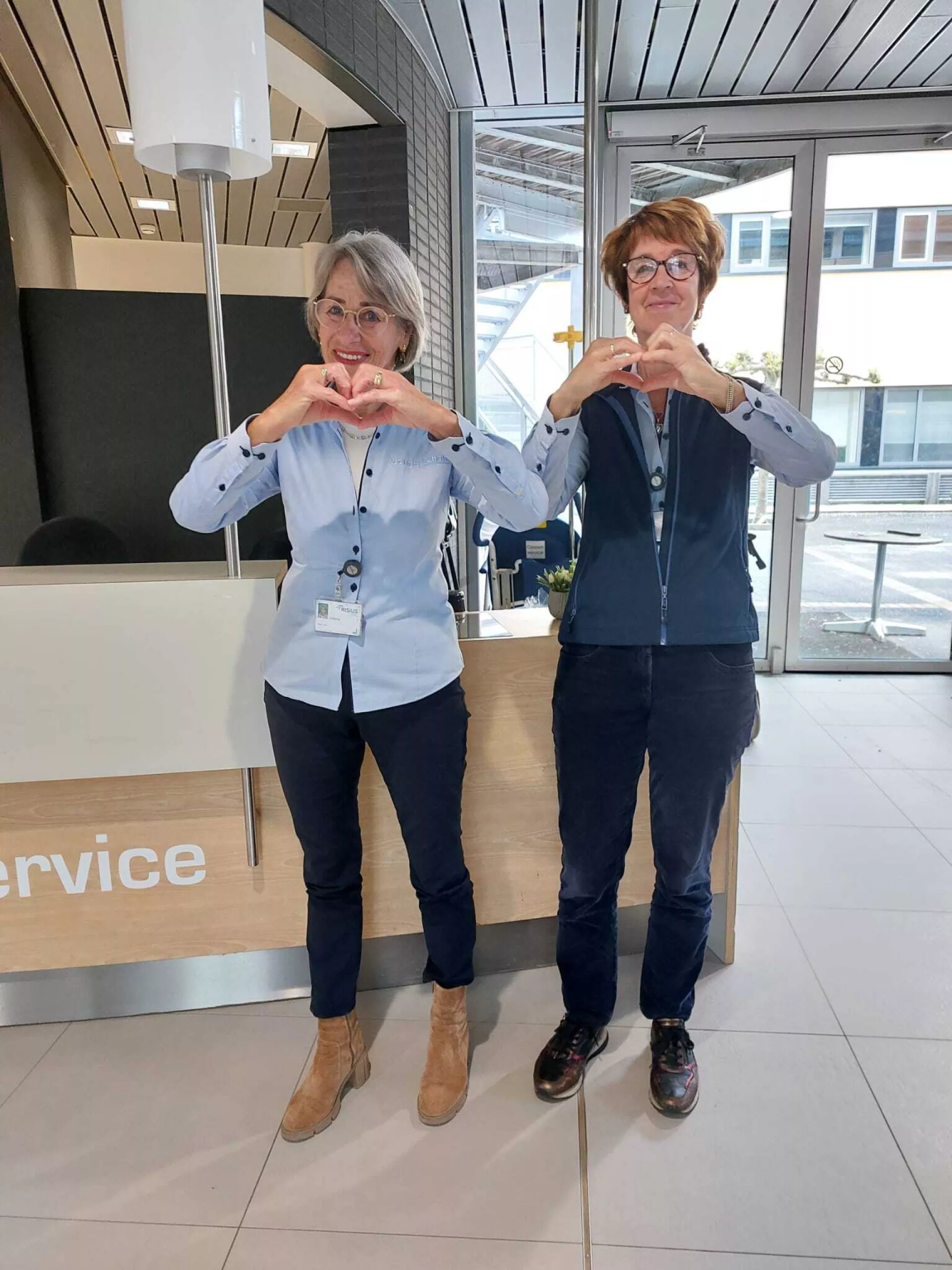 Twee vrouwen in bedrijfskleding vormen hartjes met hun handen in het ziekenhuis.