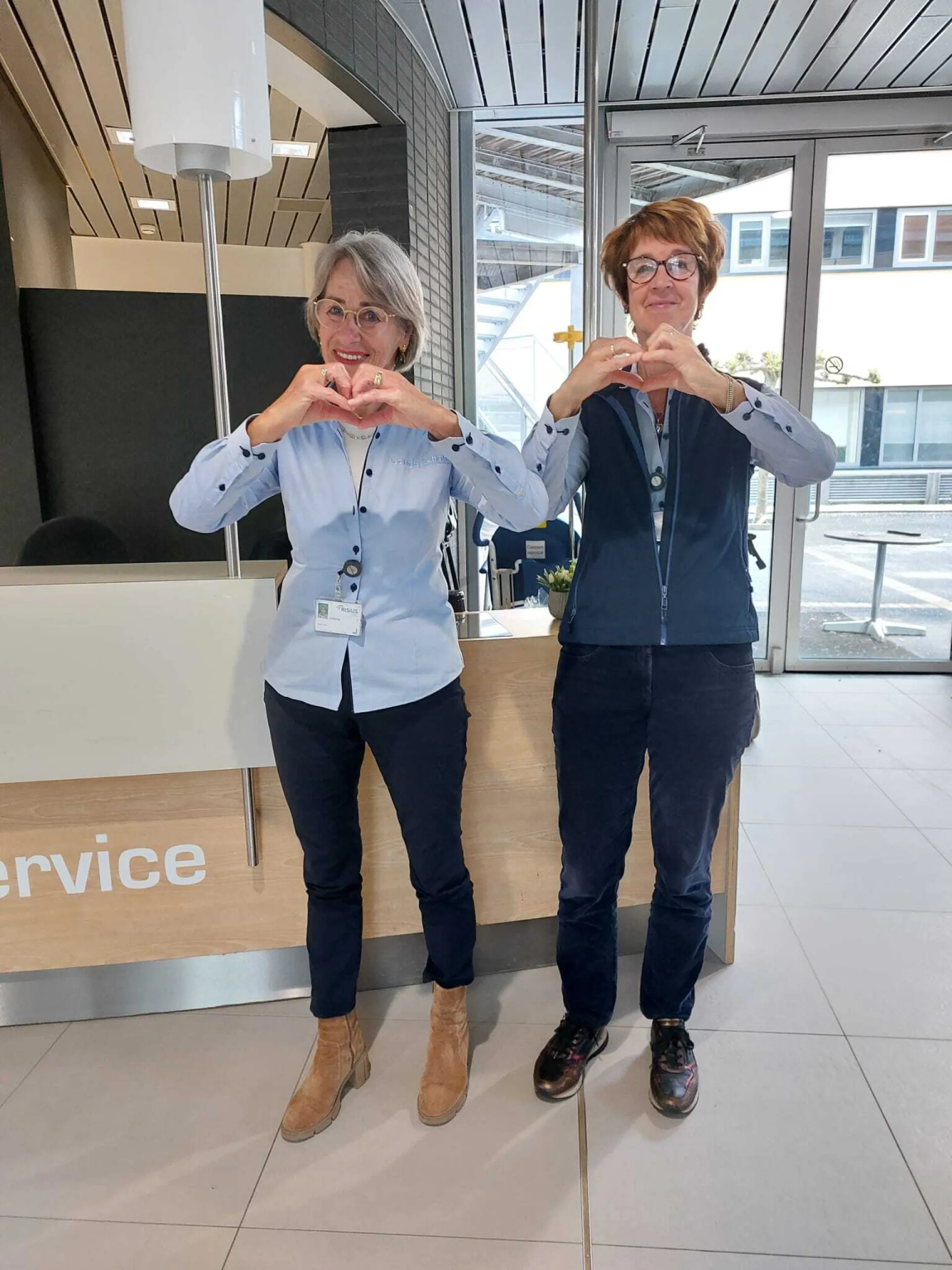 Twee vrouwen in bedrijfskleding vormen hartjes met hun handen in het ziekenhuis.
