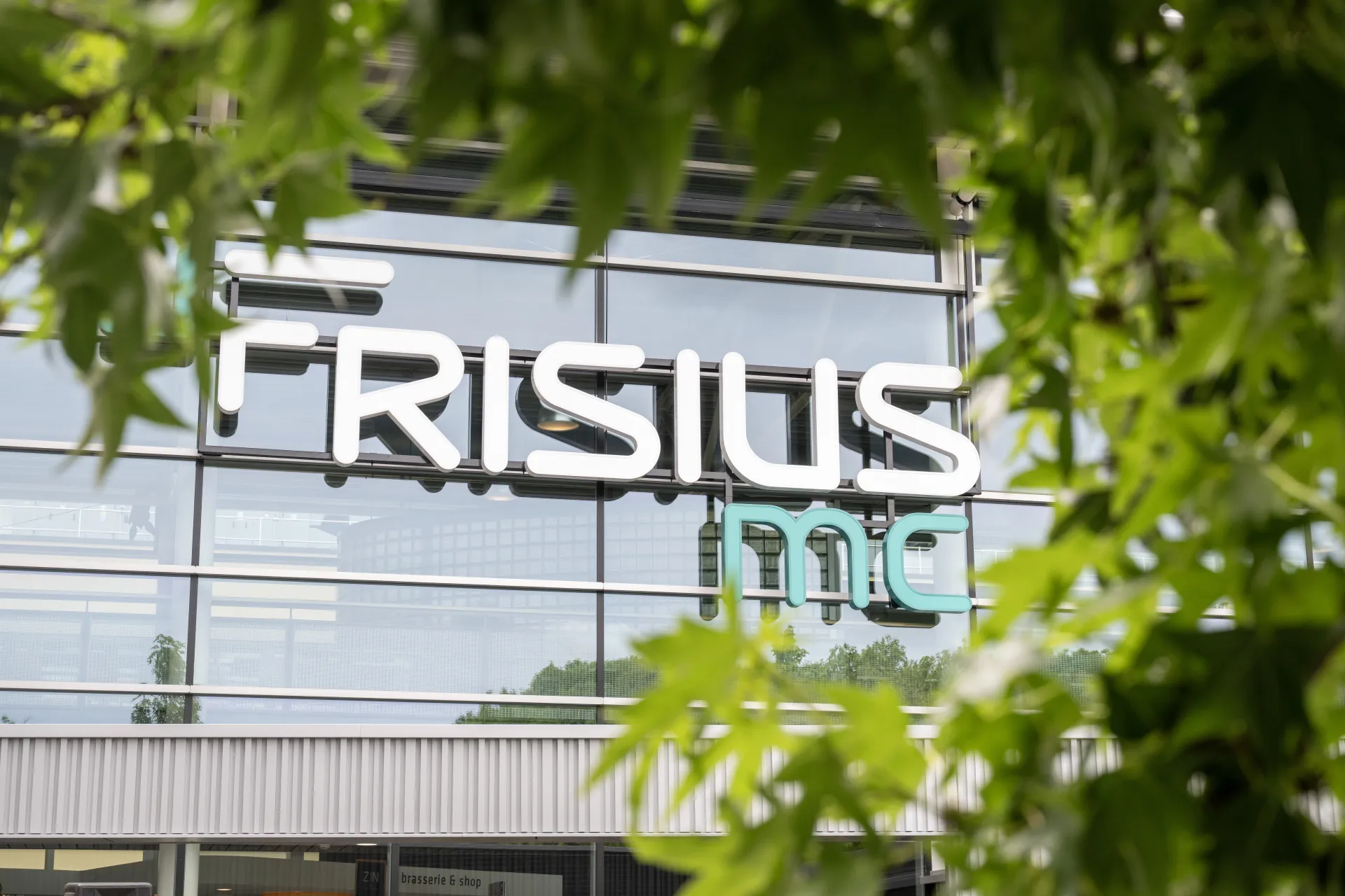 Logo van Frisius Medisch Centrum op de gevel gedeeltelijk verborgen door groene bladeren.