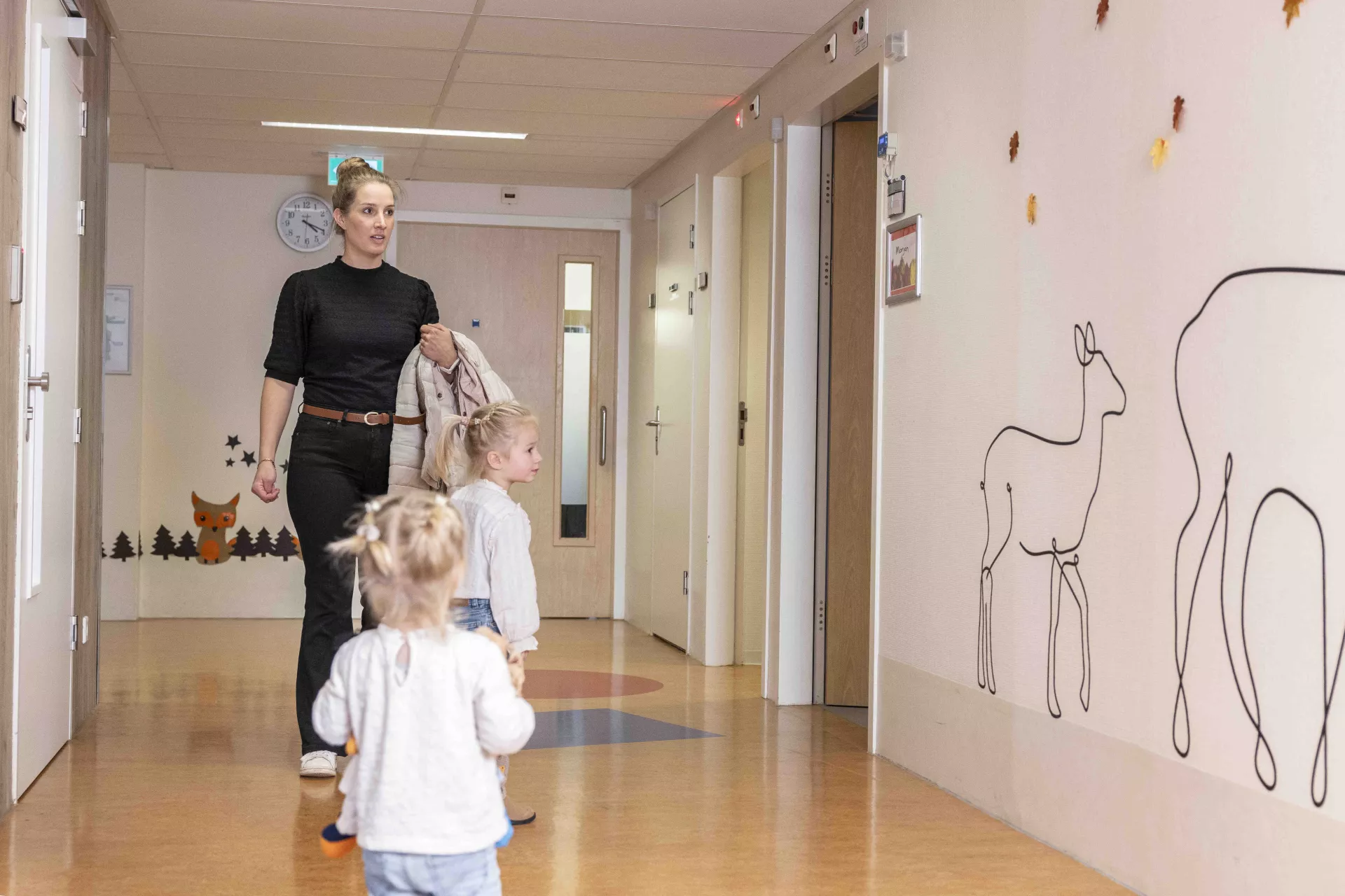 Een vrouw en twee jonge kinderen lopen door een gang van het ziekenhuis.