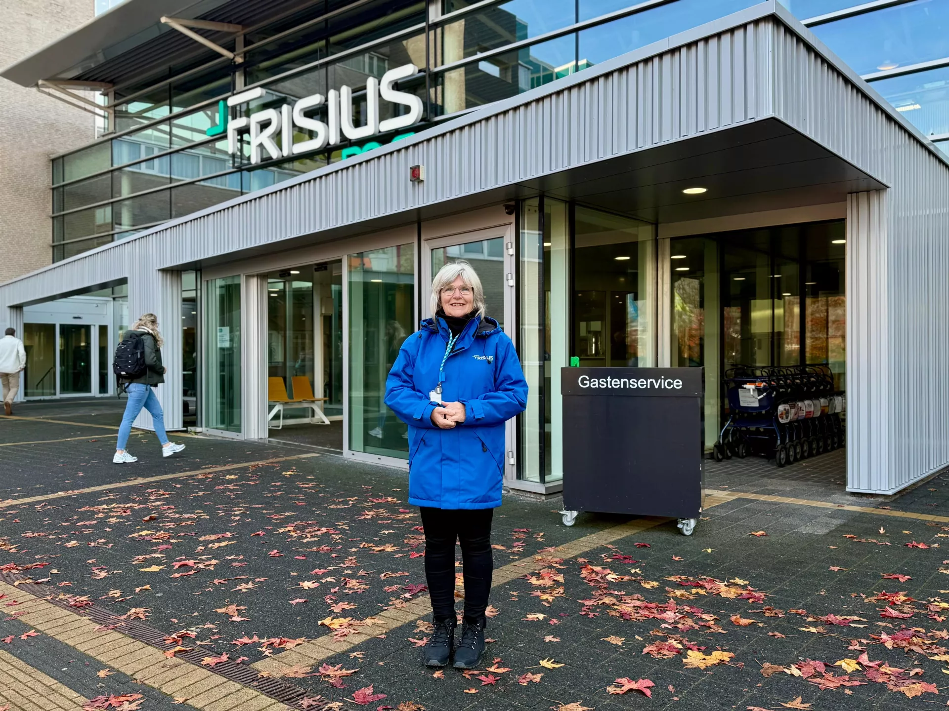 Gastvrouw in een blauwe jas staat voor het ziekenhuis.
