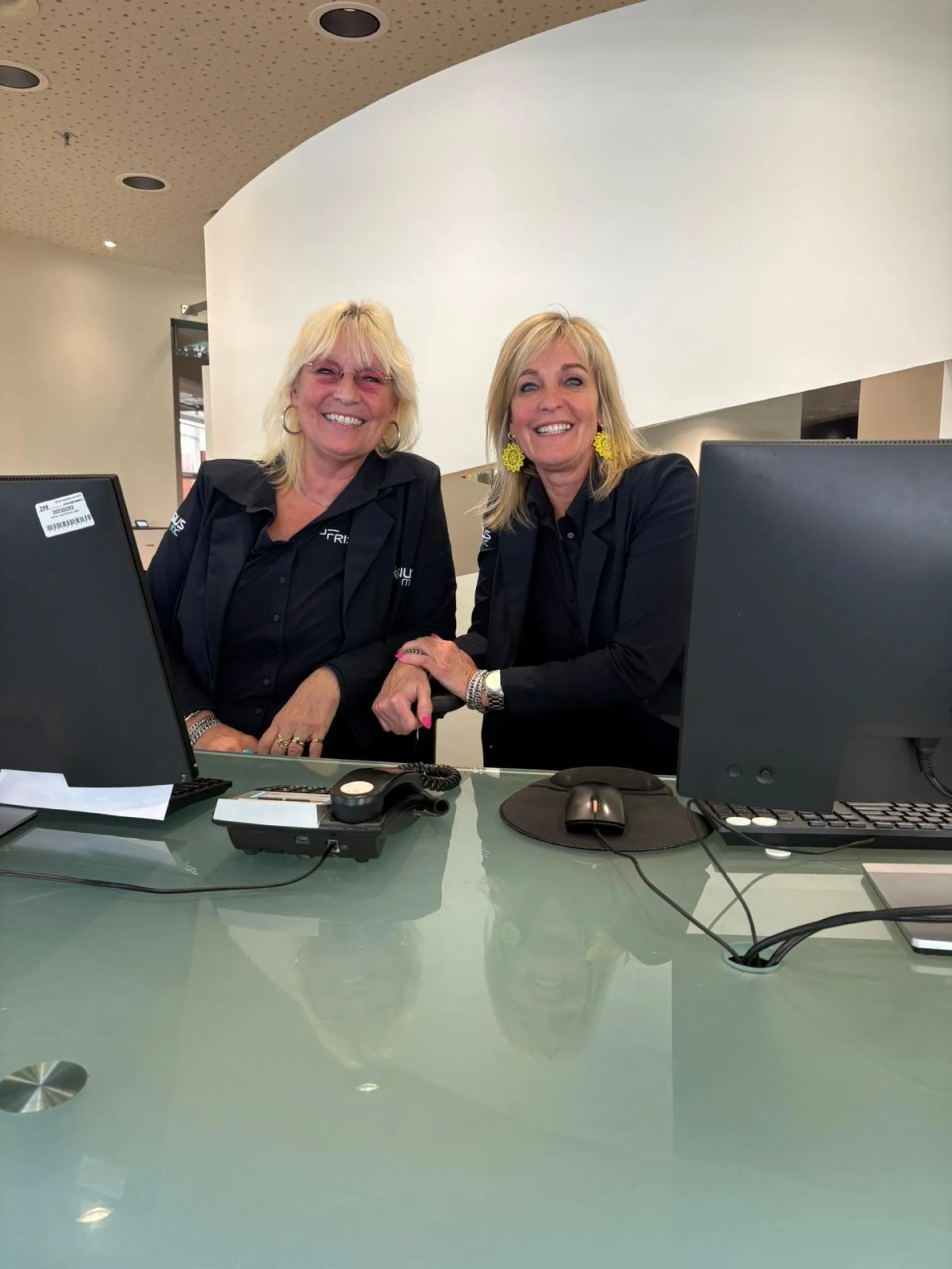 Twee medewerkers glimlachend achter de ontvangstbalie.