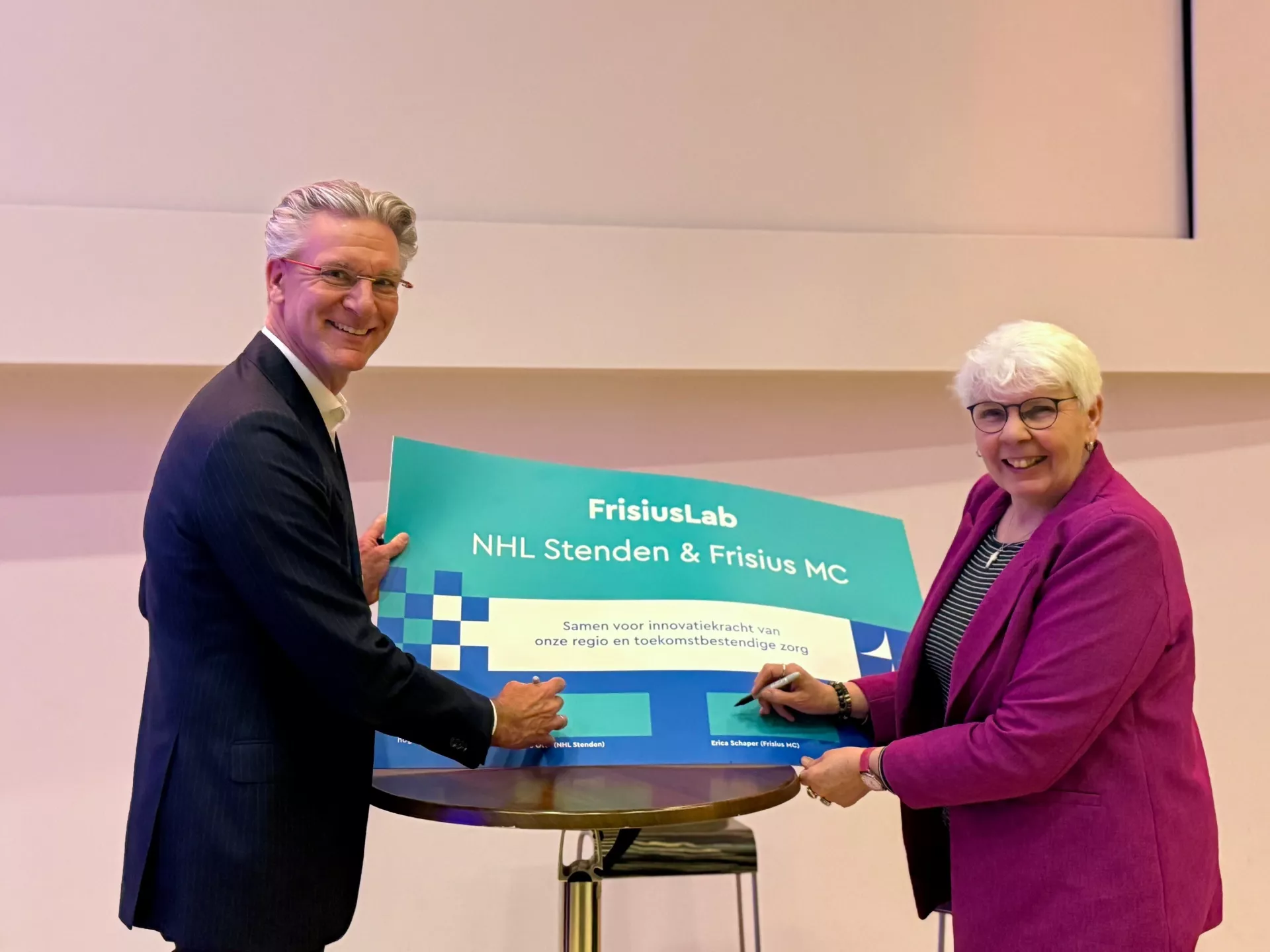 Twee personen poseren met een groot bord van FrisusLab.