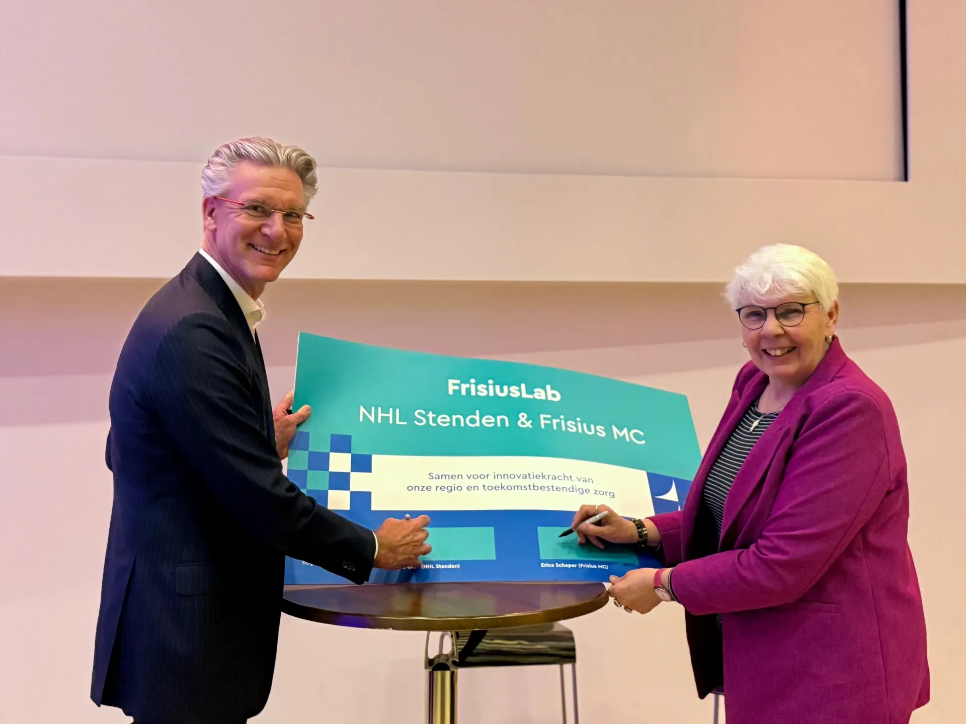 Twee personen poseren met een groot bord van FrisusLab.