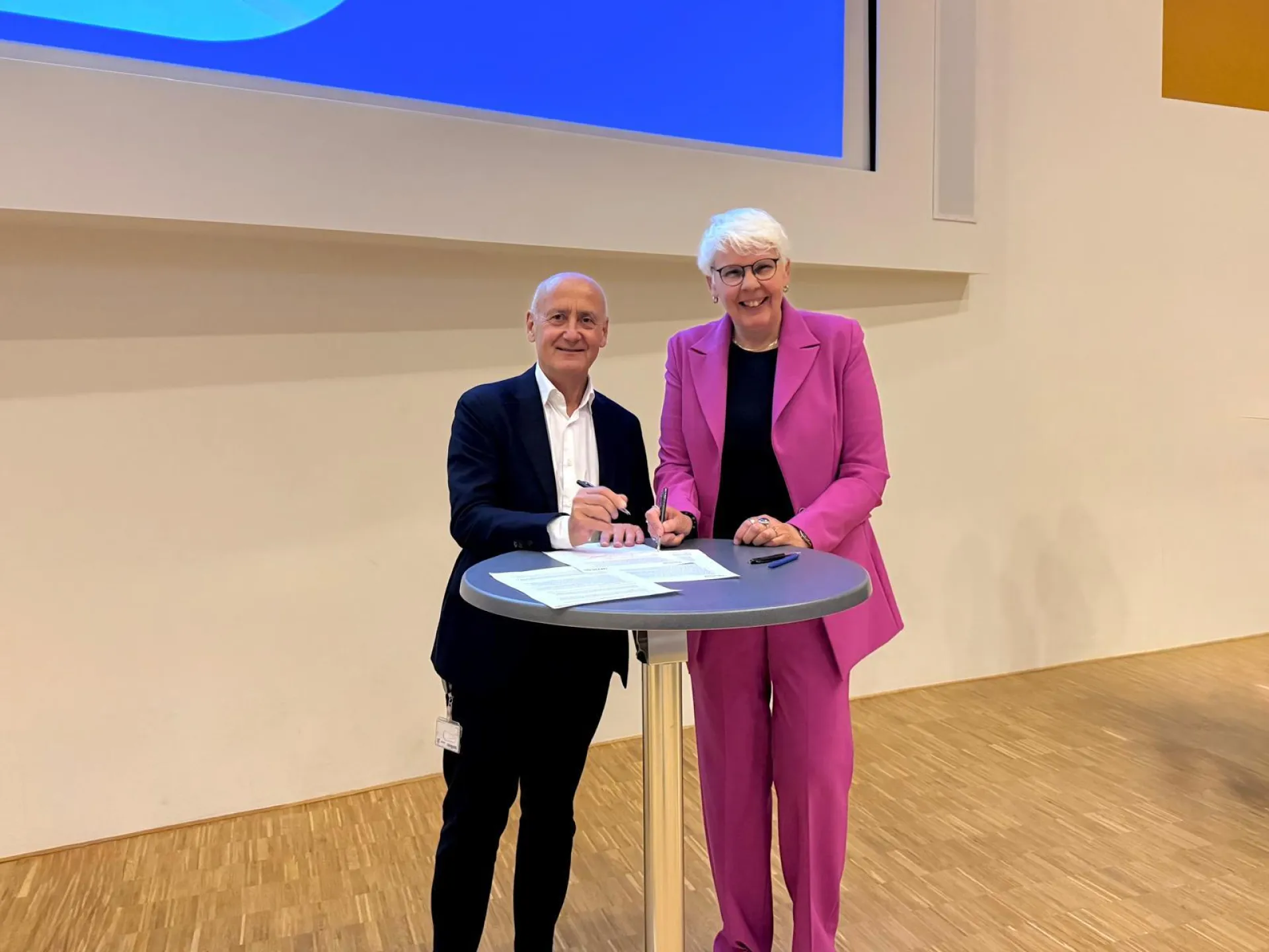 Twee bestuurders poseren samen bij een hoge tafel bij een ondertekenmoment.