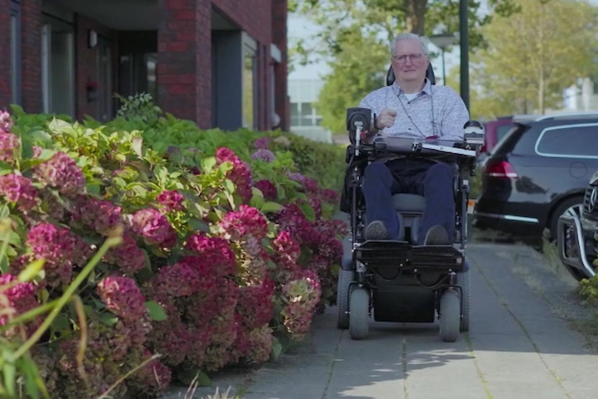 Persoon in een elektrische rolstoel rijdt over een trottoir naast kleurrijke bloemen.