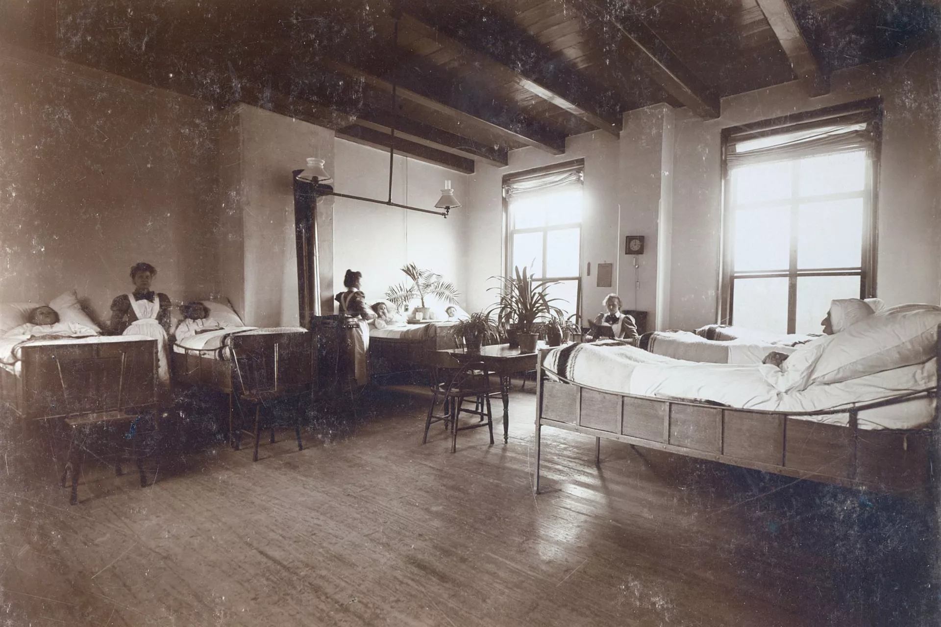Een historische foto van een gedeelde ziekenhuiskamer waar patiënten in bed liggen.