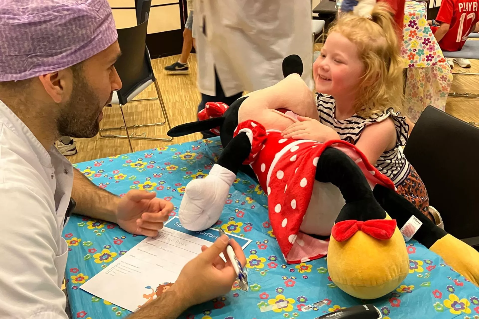 Een co-assistent in gesprek met een lachend meisje en een grote Minnie Mouse-knuffel.