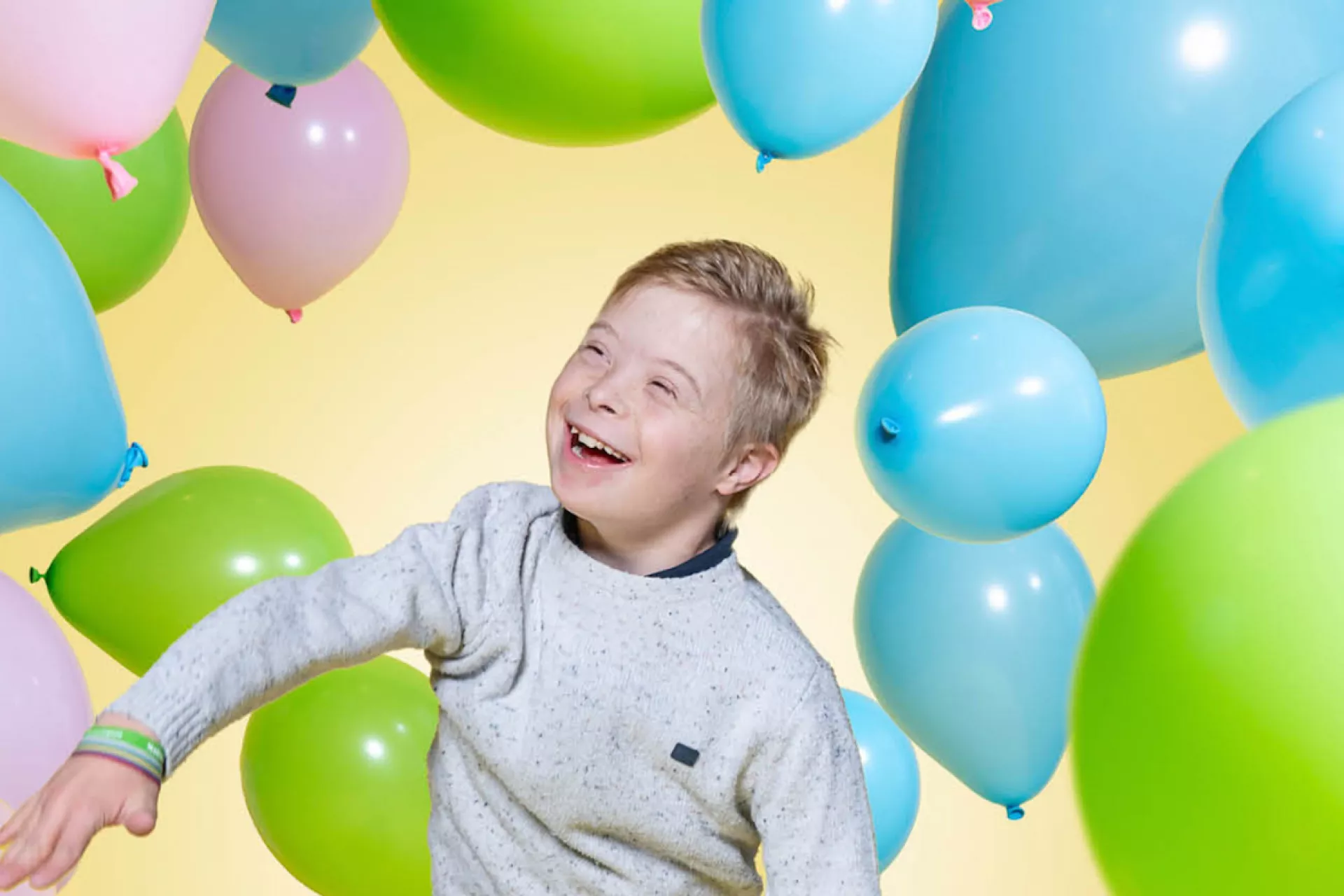 Een lachend kind tussen kleurrijke ballonnen.