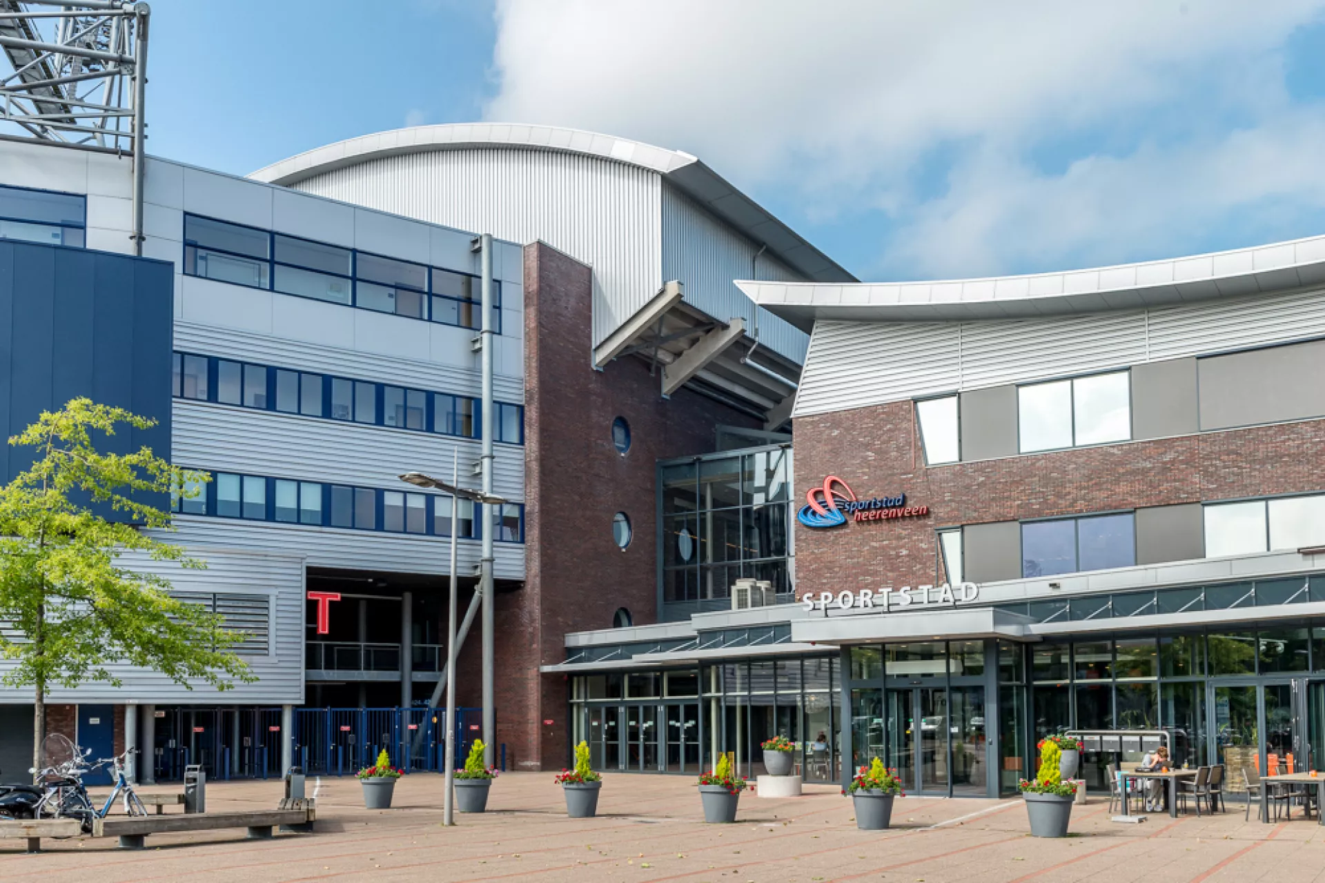 Vooraanzicht van locatie Sportstad Heerenveen met glazen entree en omliggende plantenbakken.
