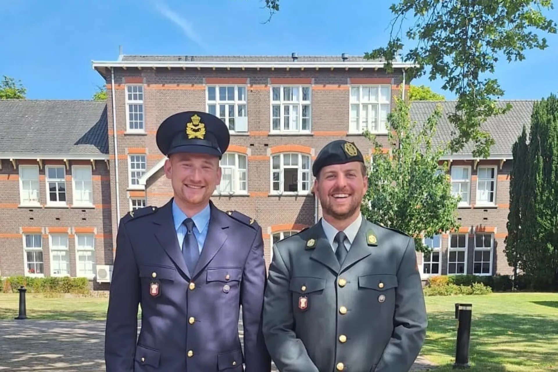 Twee mannen in militaire uniformen poseren buiten voor een gebouw.