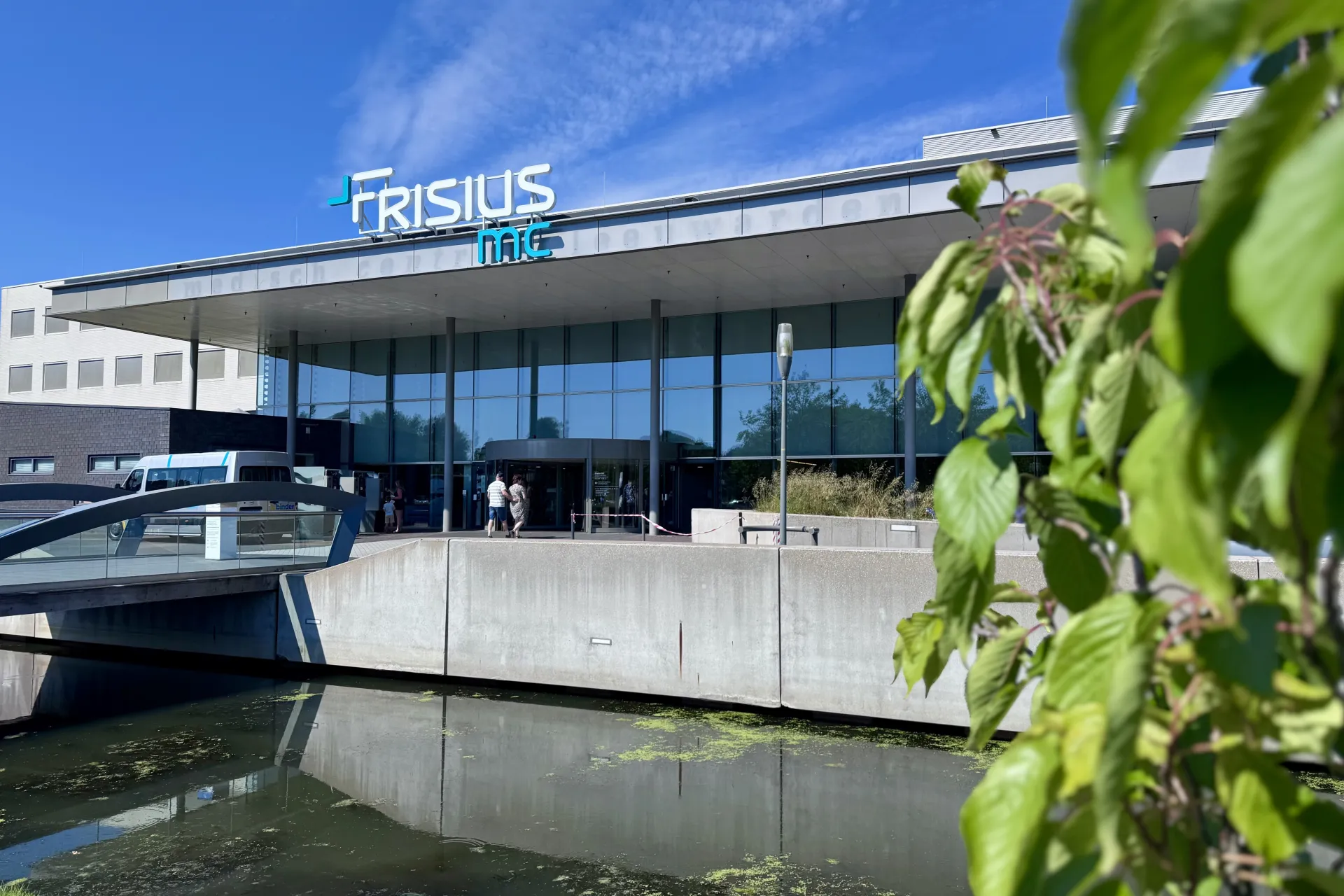 Vooraanzicht van Frisius MC Leeuwarden met een vijver op de voorgrond onder een blauwe hemel.