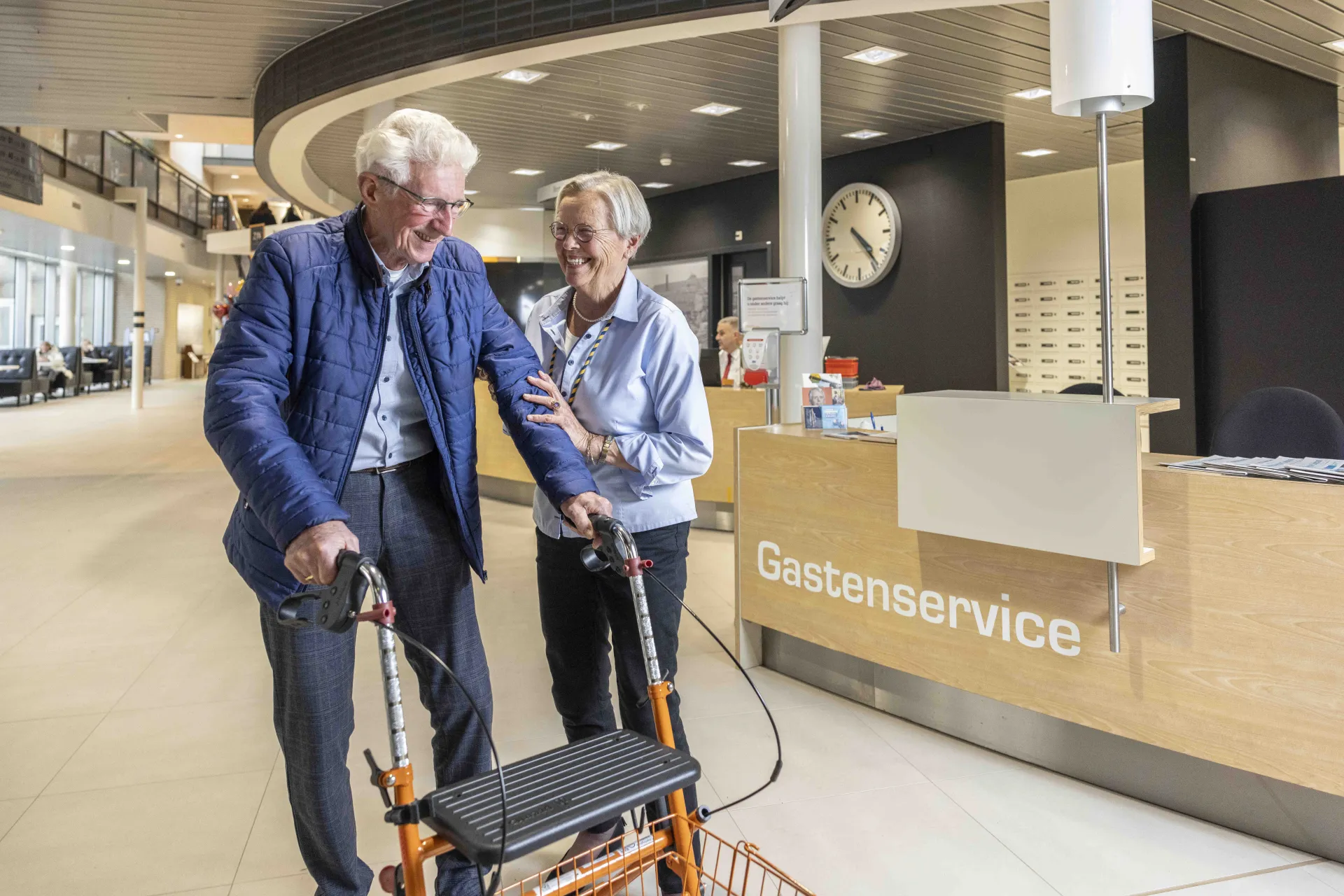 Oudere man met rollator krijgt hulp bij gastenservice.