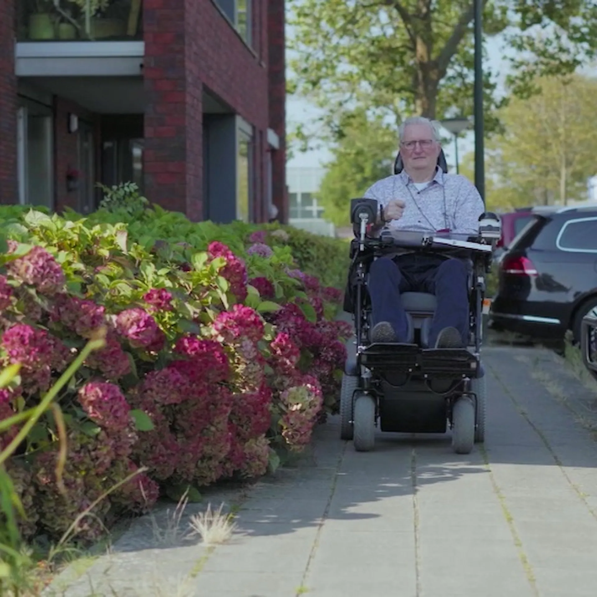 Persoon in een elektrische rolstoel rijdt over een trottoir naast kleurrijke bloemen.