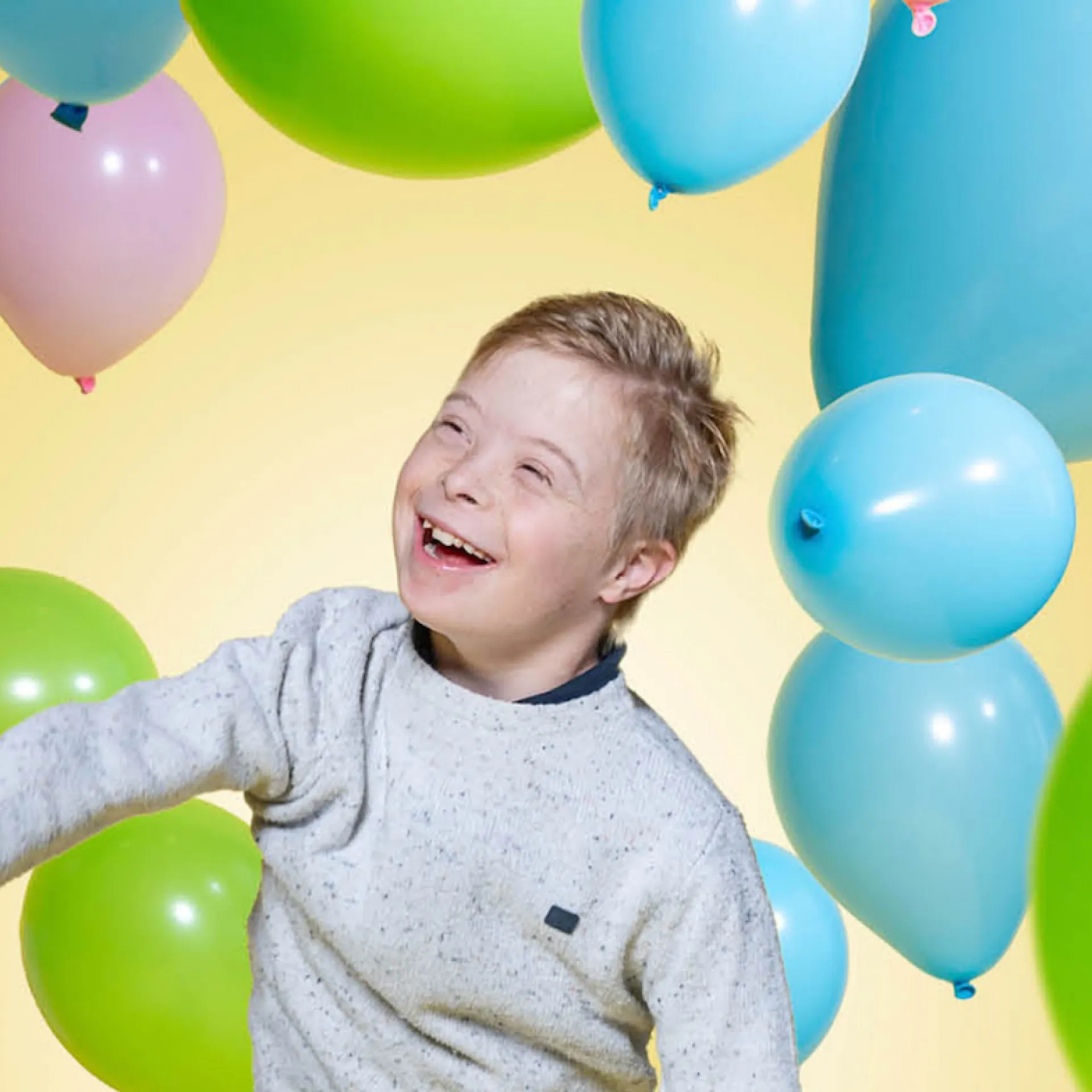 Een lachend kind tussen kleurrijke ballonnen.